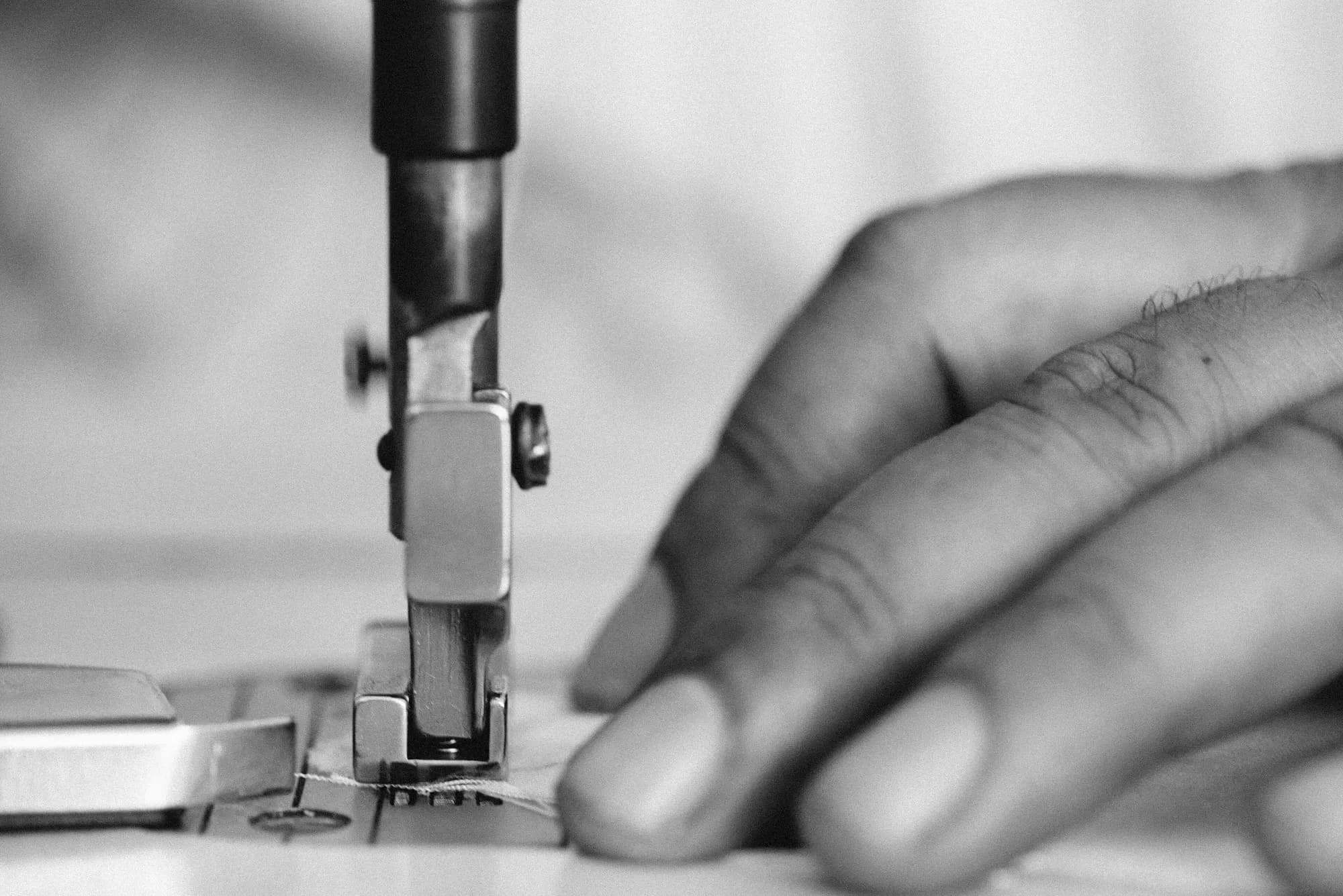 Bàn tay thợ may đưa vải qua máy may